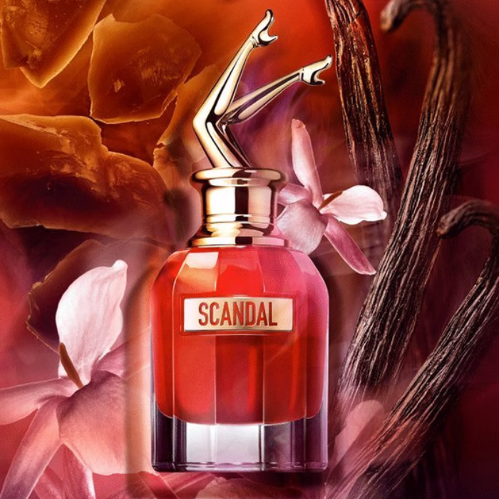 Perfume bottle labeled 'Scandal' with floral and vanilla bean elements in the background