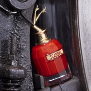 Red perfume bottle with gold cap labeled 'Scandal' on a dark textured background